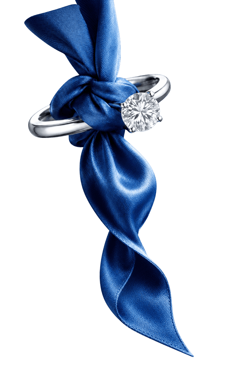 A solitaire diamond ring threaded onto a knotted blue silk ribbon